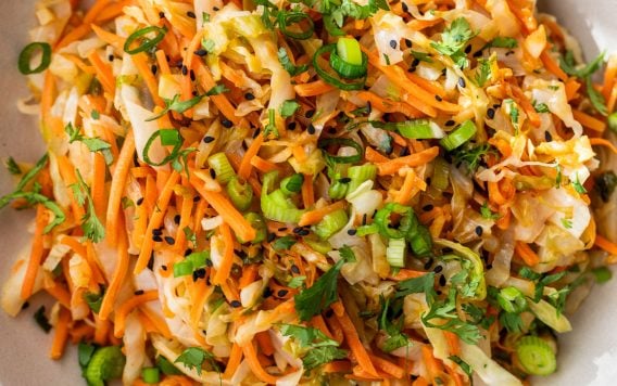 A bowl of sauteed cabbage and carrots with green onions, cilantro, and black sesame seeds.