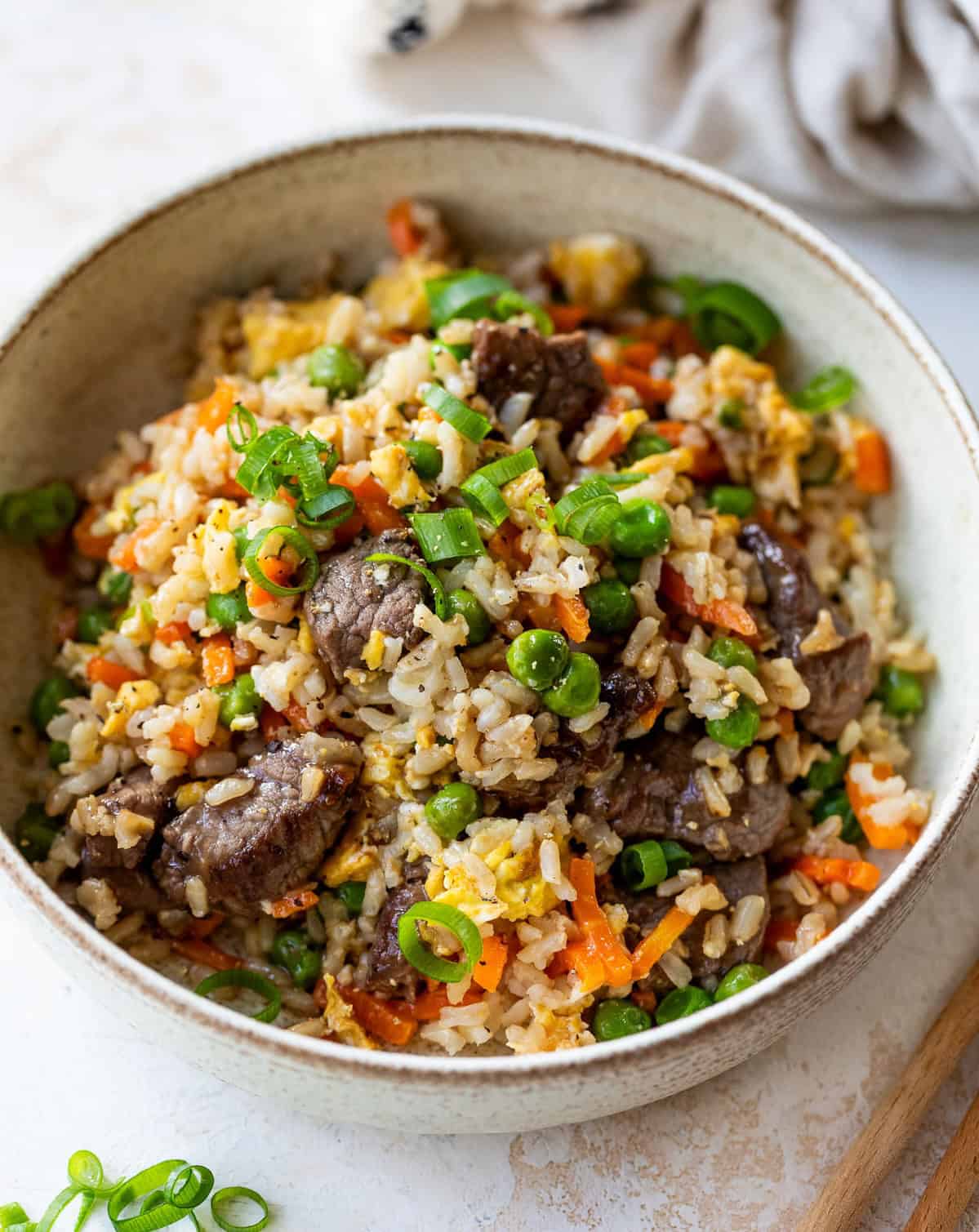 A bowl of steak fried rice with beef, peas, carrots, scrambled egg, and chopped green onions.