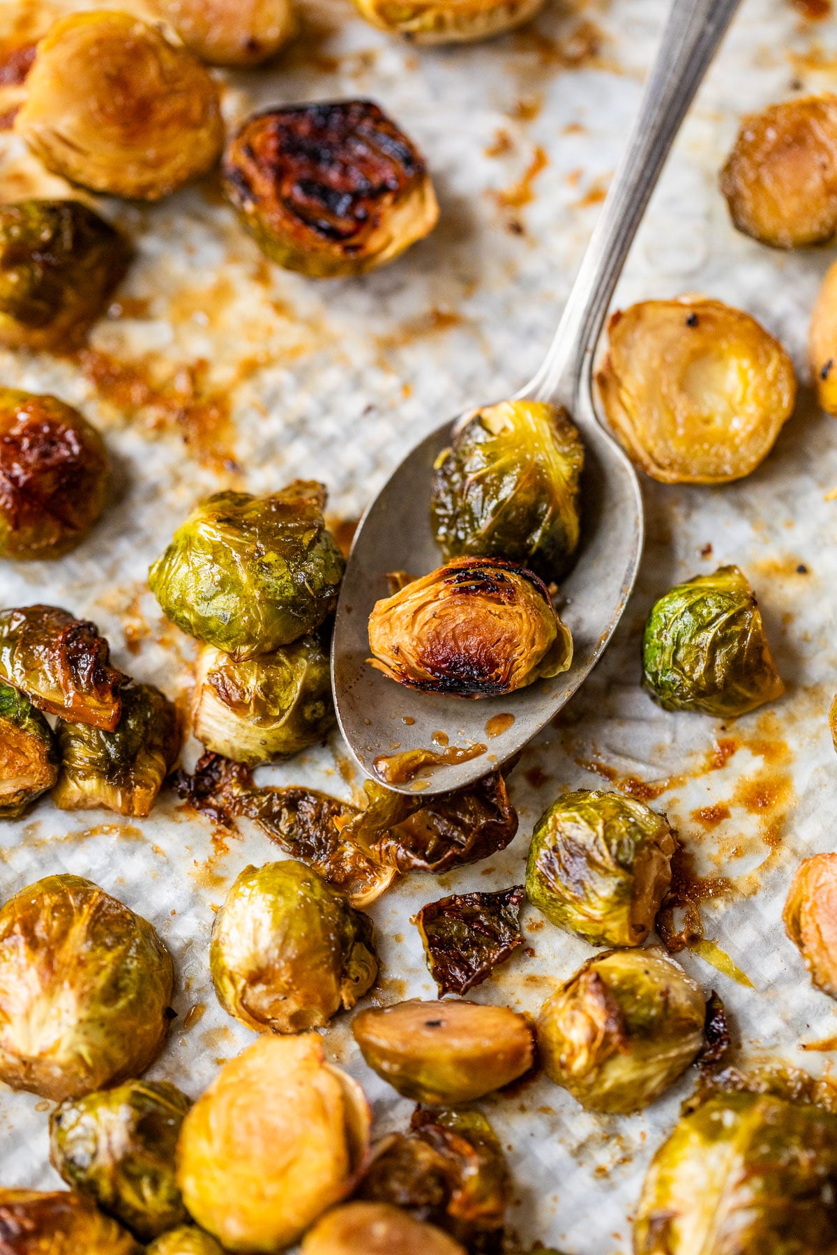 Caramelized Brussels sprouts on a baking sheet with a spoon scooping some up, showing crispy, caramelized edges.