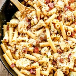 Ziti pasta with roasted cauliflower, bacon, and breadcrumbs in a skillet, mixed with a wooden spoon.