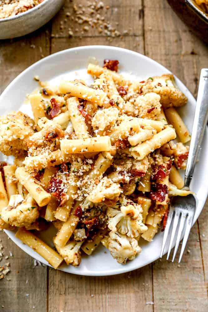 Cauliflower pasta with bacon and breadcrumbs on a white plate with a fork.
