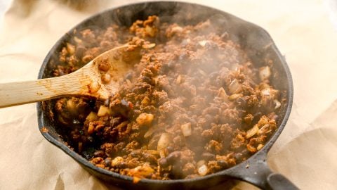 Steaming skillet of seasoned ground beef and chopped onions being stirred with a wooden spoon.