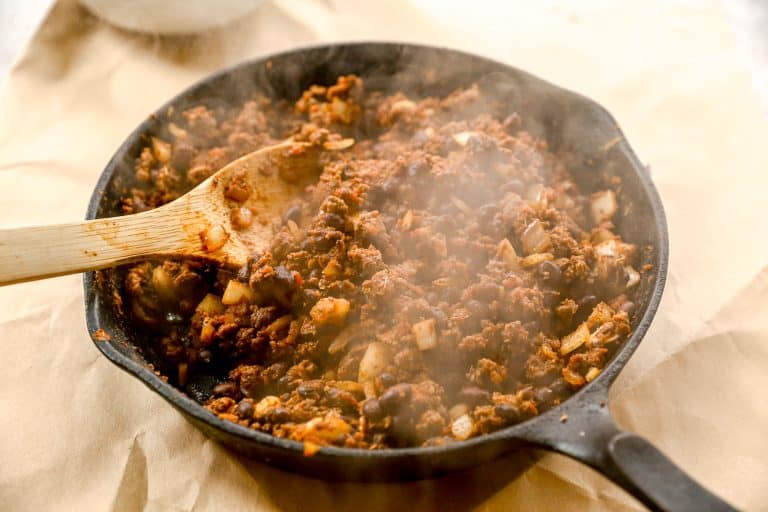 Steaming skillet of seasoned ground beef and chopped onions being stirred with a wooden spoon.