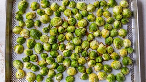 Halved Brussels sprouts spread on a parchment-lined baking sheet, ready to be roasted.