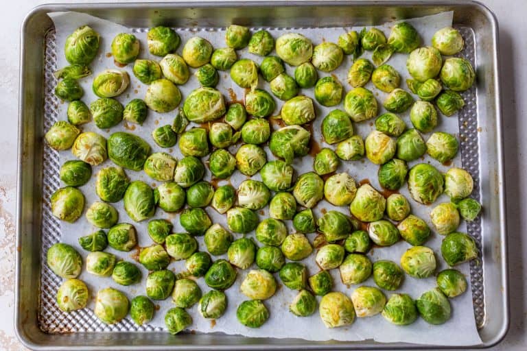 Halved Brussels sprouts spread on a parchment-lined baking sheet, ready to be roasted.