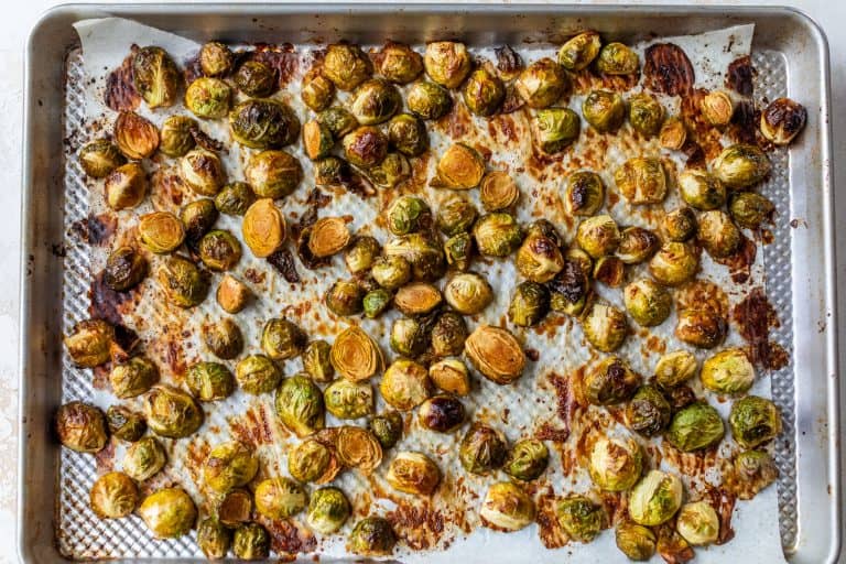 Caramelized Brussels sprouts on a parchment-lined baking sheet, browned and caramelized after baking.
