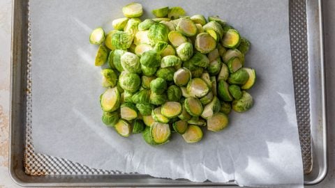 Halved Brussels sprouts piled on a parchment-lined baking sheet, ready for roasting.