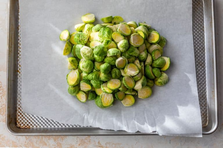 Halved Brussels sprouts piled on a parchment-lined baking sheet, ready for roasting.