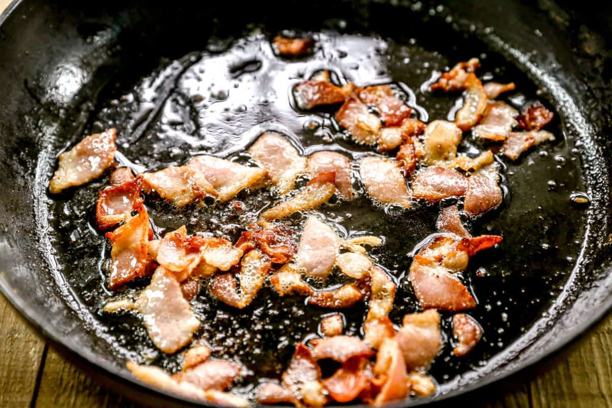 Crispy bacon pieces frying in a black skillet with sizzling grease on the surface.