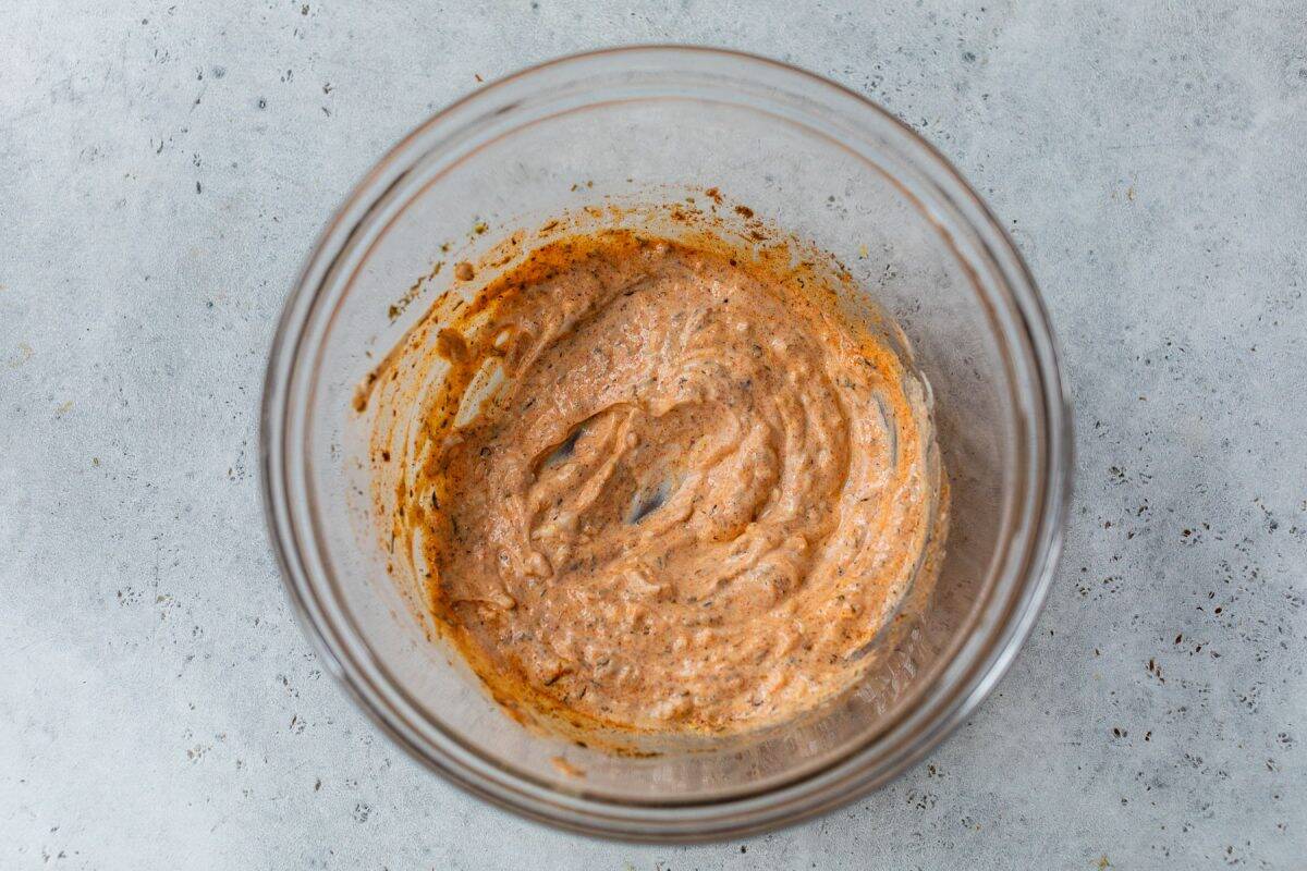 Spiced creamy marinade in a glass bowl on a gray textured surface, viewed from above.