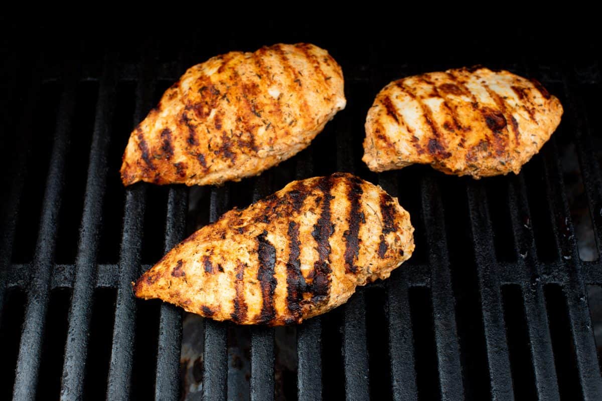 Three seasoned chicken breasts with grill marks cooking on a black grill grate.