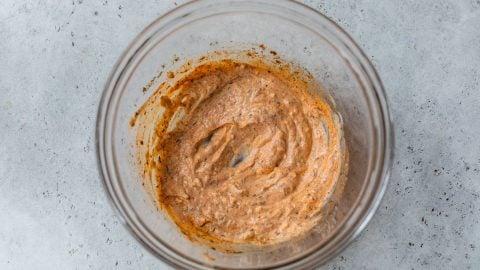 Spiced creamy marinade in a glass bowl on a gray textured surface, viewed from above.