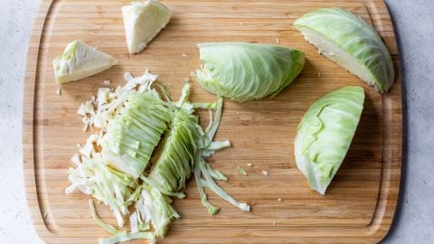 Chopped and sliced green cabbage on a wooden cutting board.