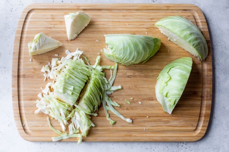 Chopped and sliced green cabbage on a wooden cutting board.