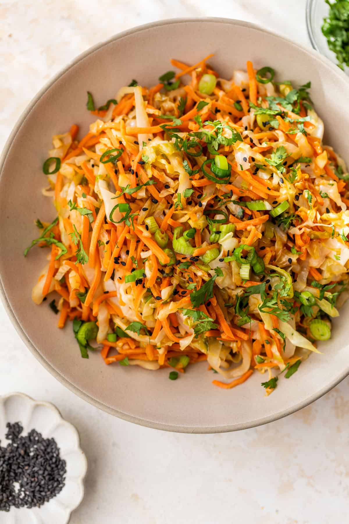 Bowl of sauteed cabbage and carrots with green onions, cilantro, and black sesame seeds.