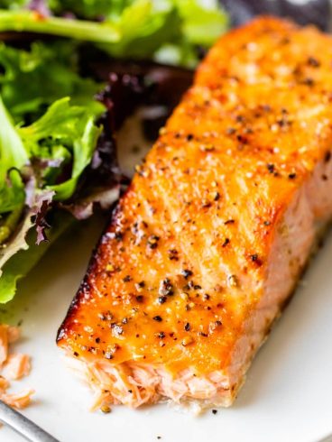 A piece of seasoned baked salmon with a side of mixed green salad on a white plate.