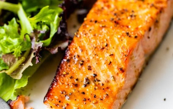 A piece of seasoned baked salmon with a side of mixed green salad on a white plate.