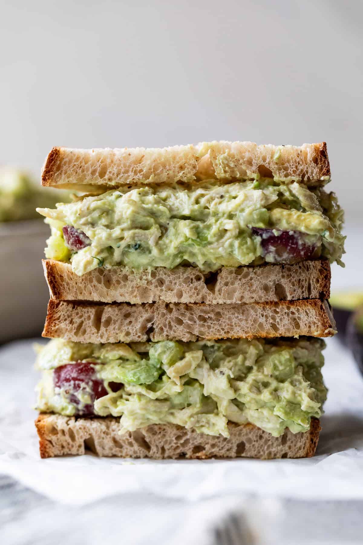 Two halves of a sandwich filled with creamy avocado chicken salad, stacked on top of each other on whole grain bread.