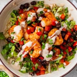 A shrimp bowl with black beans, red peppers, lettuce, green onions, and sauce served over quinoa.