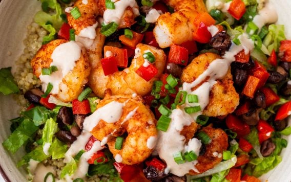 A shrimp bowl with black beans, red peppers, lettuce, green onions, and sauce served over quinoa.
