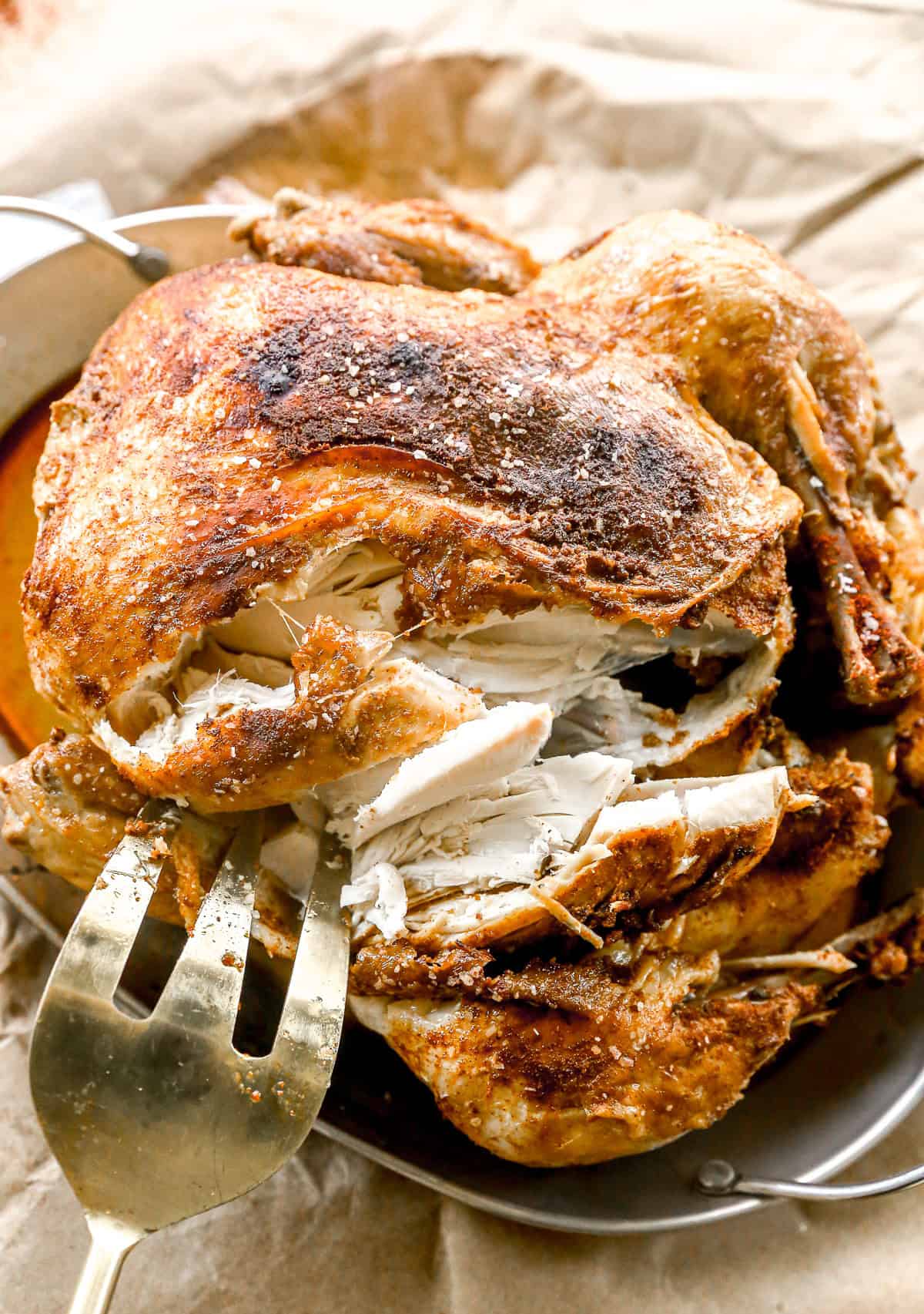 A fork slices into a seasoned, crockpot whole chicken on a plate lined with parchment paper.