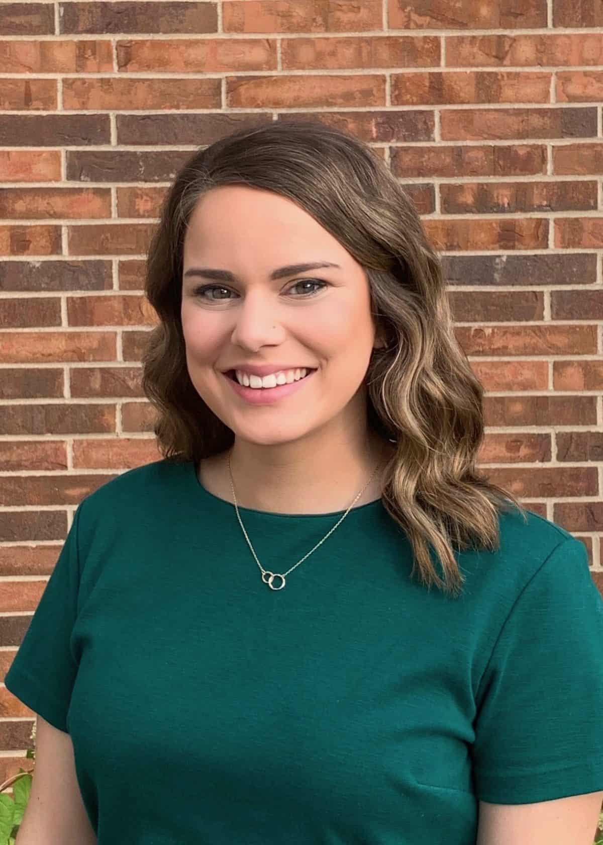 Woman in a green shirt smiling with a brick wall background.
