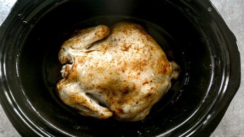 Whole seasoned chicken in a black slow cooker, ready to be cooked.