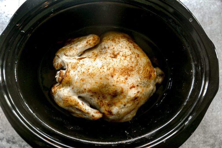 Whole seasoned chicken in a black slow cooker, ready to be cooked.