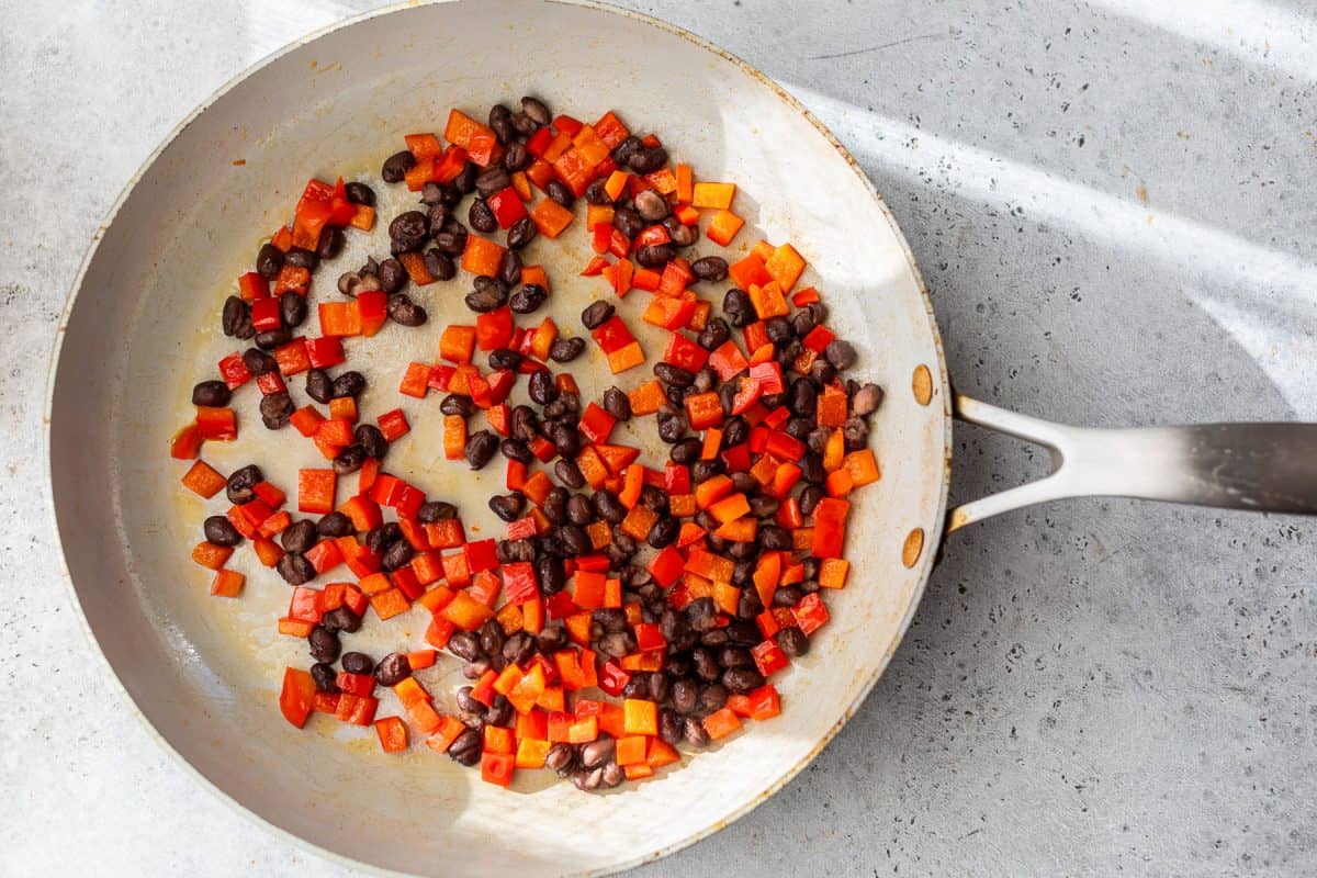 A skillet with sautéed black beans and diced red bell peppers on a light gray countertop.
