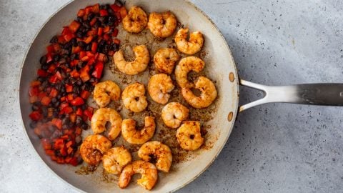 Shrimp and diced vegetables cooking in a skillet on a gray countertop.