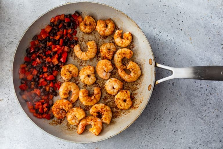 Shrimp and diced vegetables cooking in a skillet on a gray countertop.