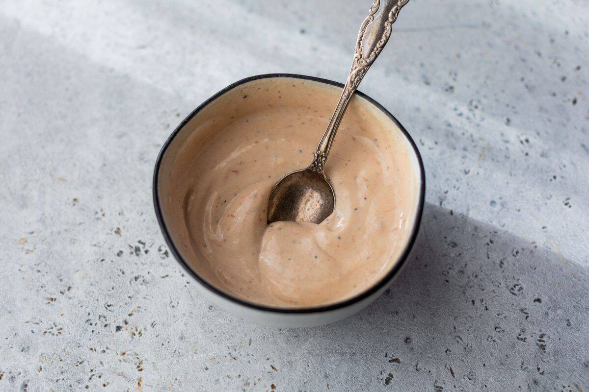 A small bowl of creamy BBQ yogurt sauce with a spoon in it, on a light textured surface.