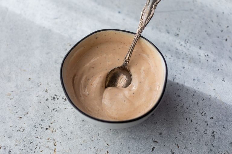 A small bowl of creamy BBQ yogurt sauce with a spoon in it, on a light textured surface.
