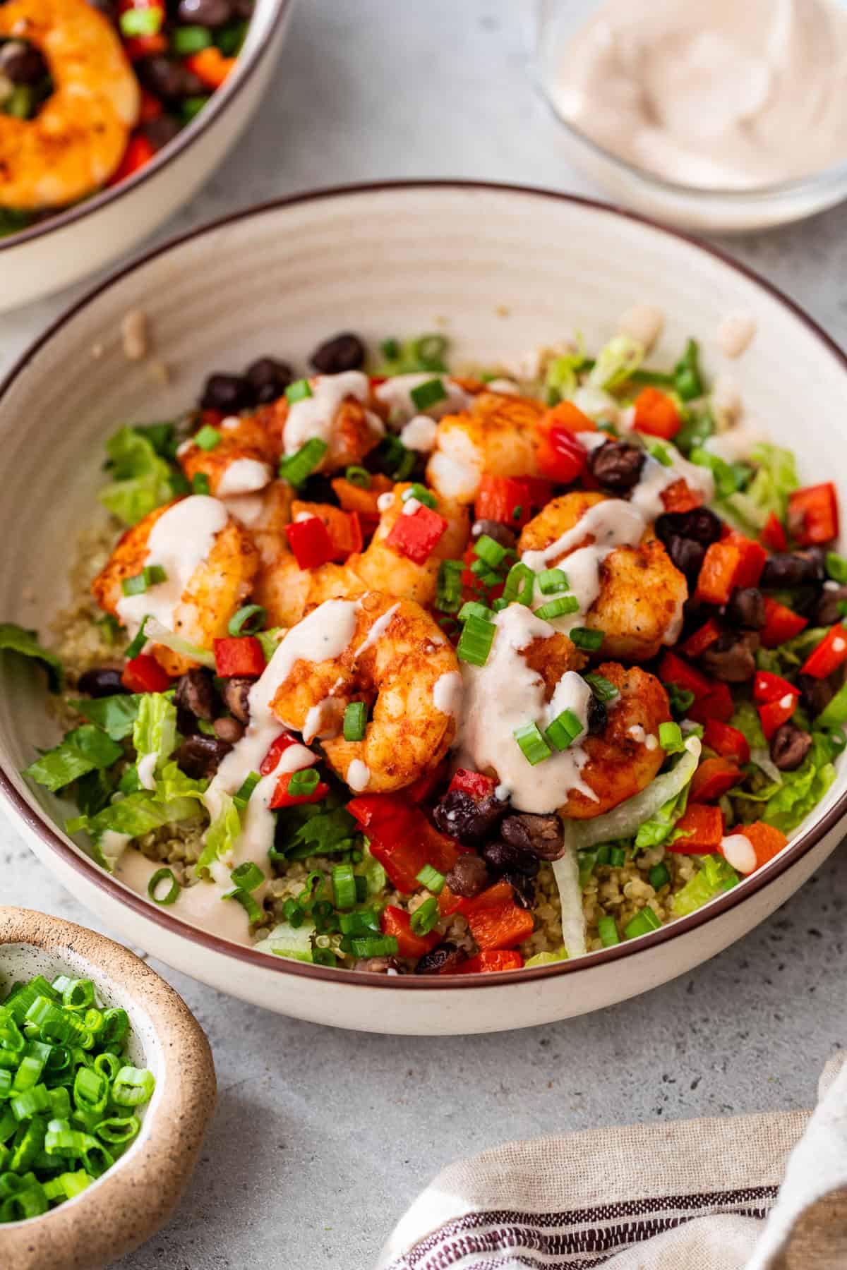 A shrimp bowl with black beans, diced red peppers, lettuce, green onions, and creamy sauce over rice or grains.