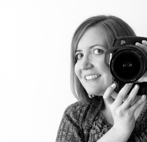 Black and white portrait of a woman holding a Canon camera.