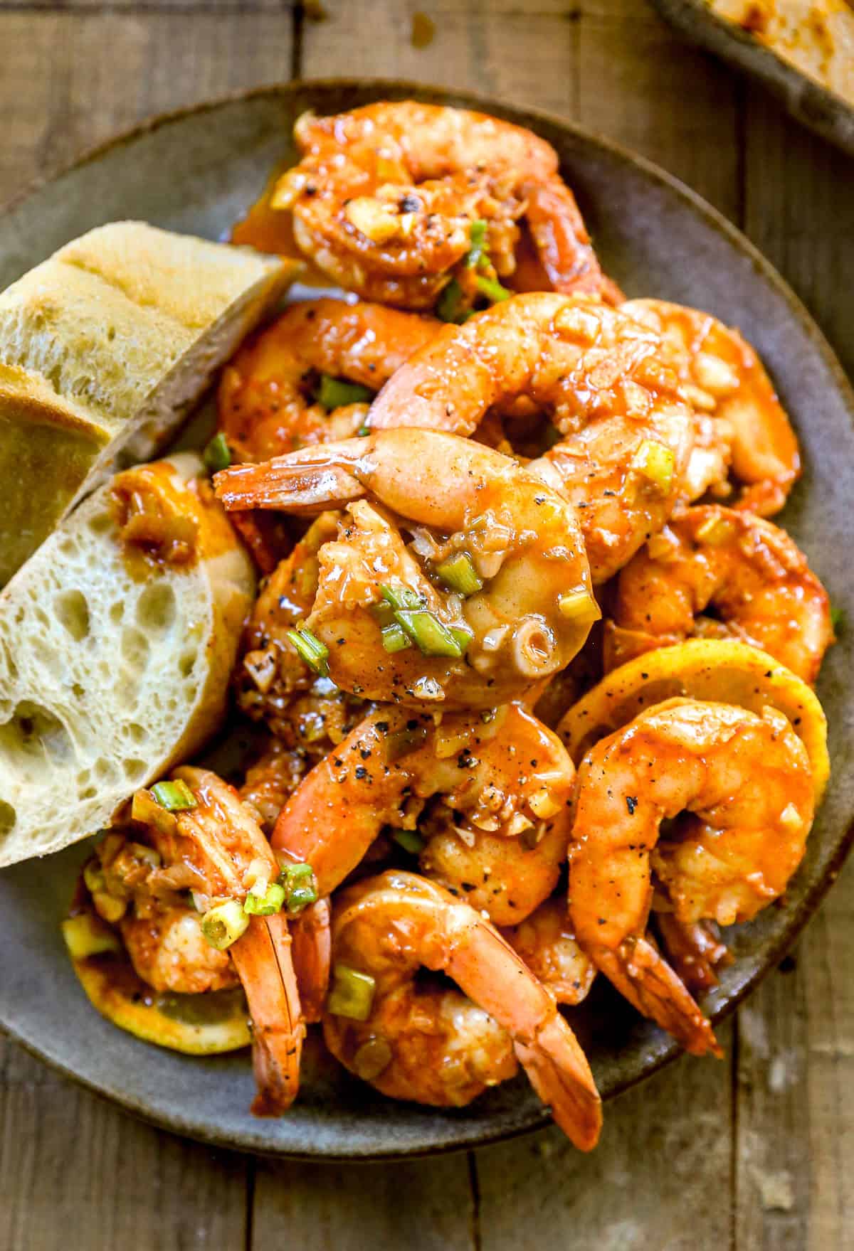 BBQ shrimp in a spicy sauce served on a plate with slices of rustic bread.