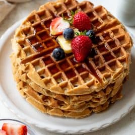 Stack of waffles topped with butter, syrup, strawberries, and blueberries on a white plate.