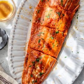 Honey mustard salmon fillet garnished with herbs, served on a white platter with a small glass of sauce nearby.