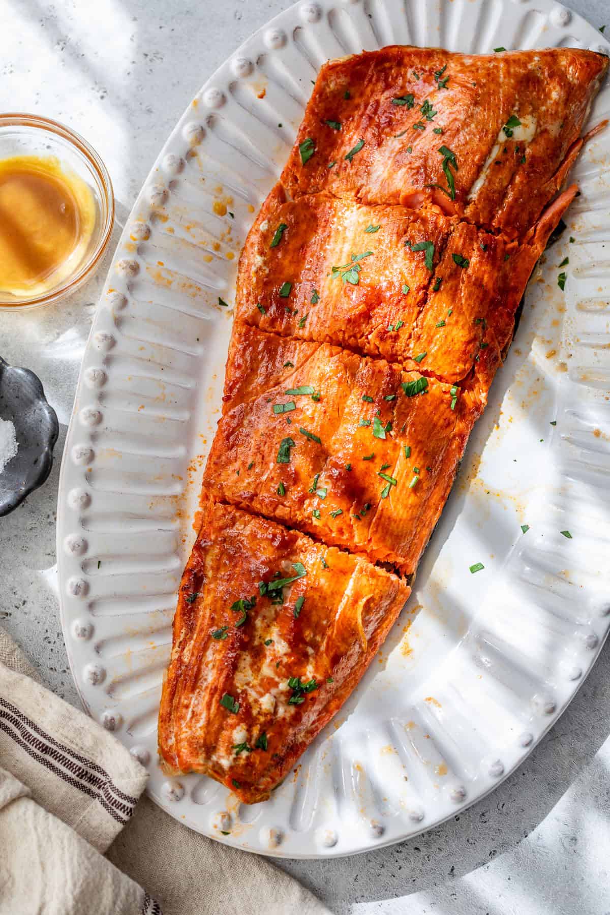 Honey mustard salmon fillet garnished with herbs, served on a white platter with a small glass of sauce nearby.