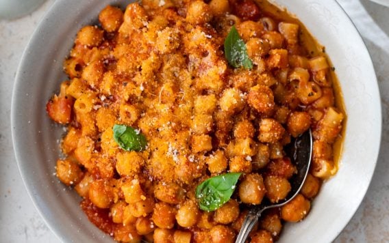 A bowl of pasta e ceci, topped with grated cheese and basil, with a spoon in the bowl.