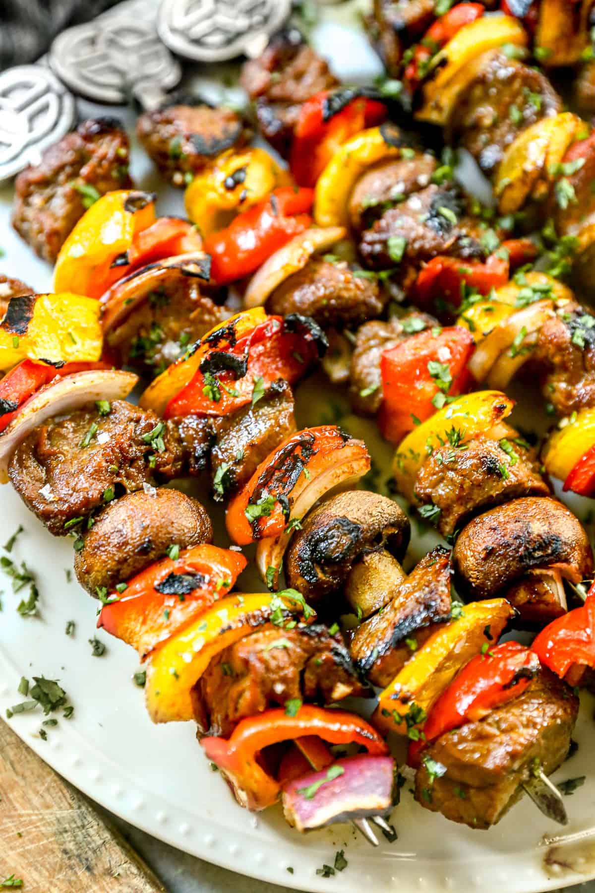 Grilled steak kabobs with peppers, onions, and mushrooms on a white plate, sprinkled with herbs.