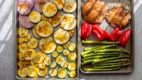 Sliced eggplant, onion, squash, zucchini, mushrooms, red bell peppers, and asparagus arranged on baking sheets.