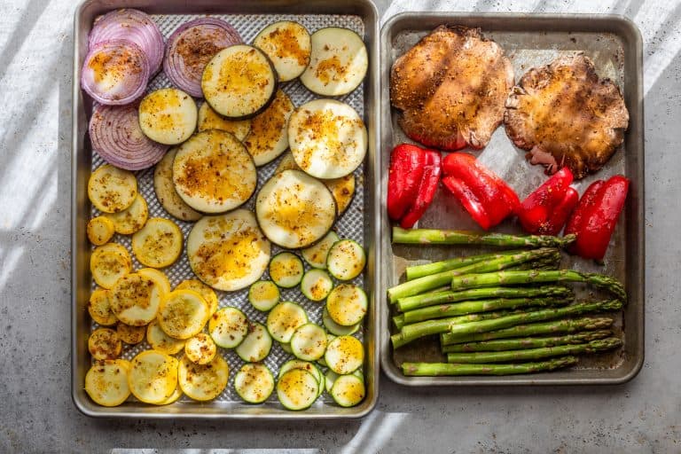 Sliced eggplant, onion, squash, zucchini, mushrooms, red bell peppers, and asparagus arranged on baking sheets.