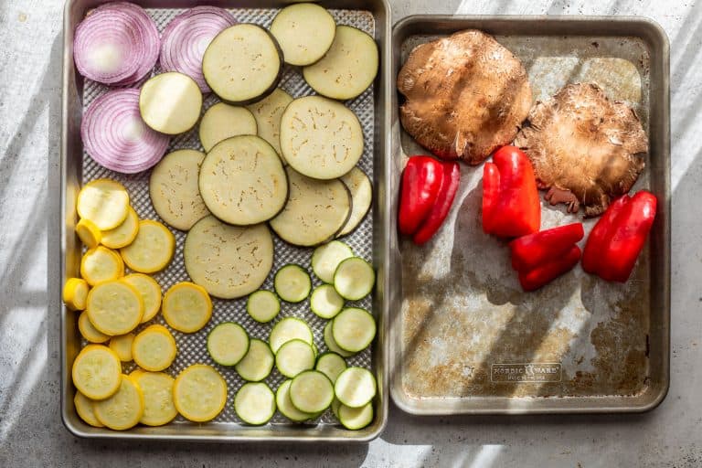 Sliced onions, eggplant, yellow squash, and zucchini on one tray; portobello mushrooms and red bell peppers on another.