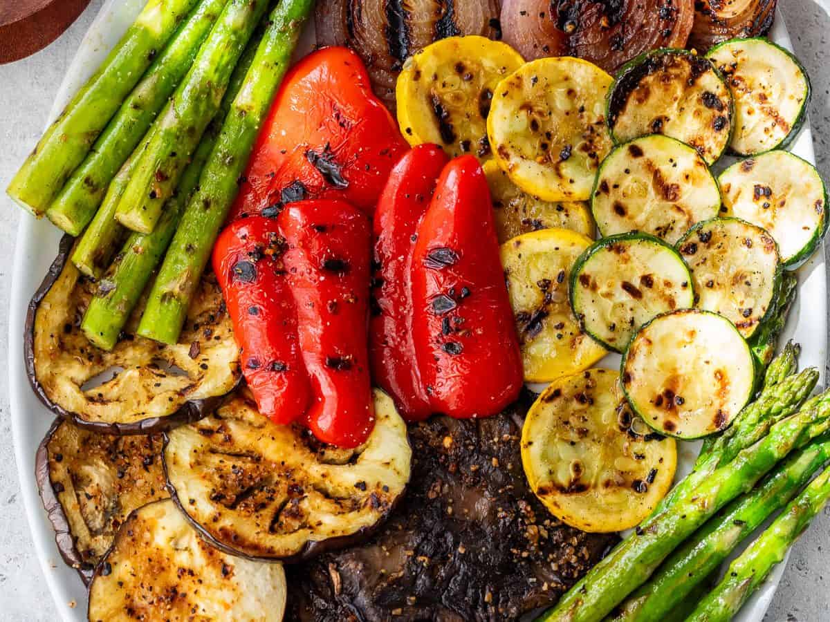 An oval platter with grilled vegetables, including asparagus, red onion, red pepper, zucchini, yellow squash, eggplant, and portobello mushrooms.