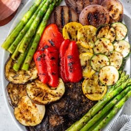 An oval platter with grilled vegetables, including asparagus, red onion, red pepper, zucchini, yellow squash, eggplant, and portobello mushrooms.