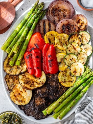 An oval platter with grilled vegetables, including asparagus, red onion, red pepper, zucchini, yellow squash, eggplant, and portobello mushrooms.