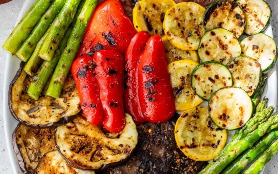 An oval platter with grilled vegetables, including asparagus, red onion, red pepper, zucchini, yellow squash, eggplant, and portobello mushrooms.