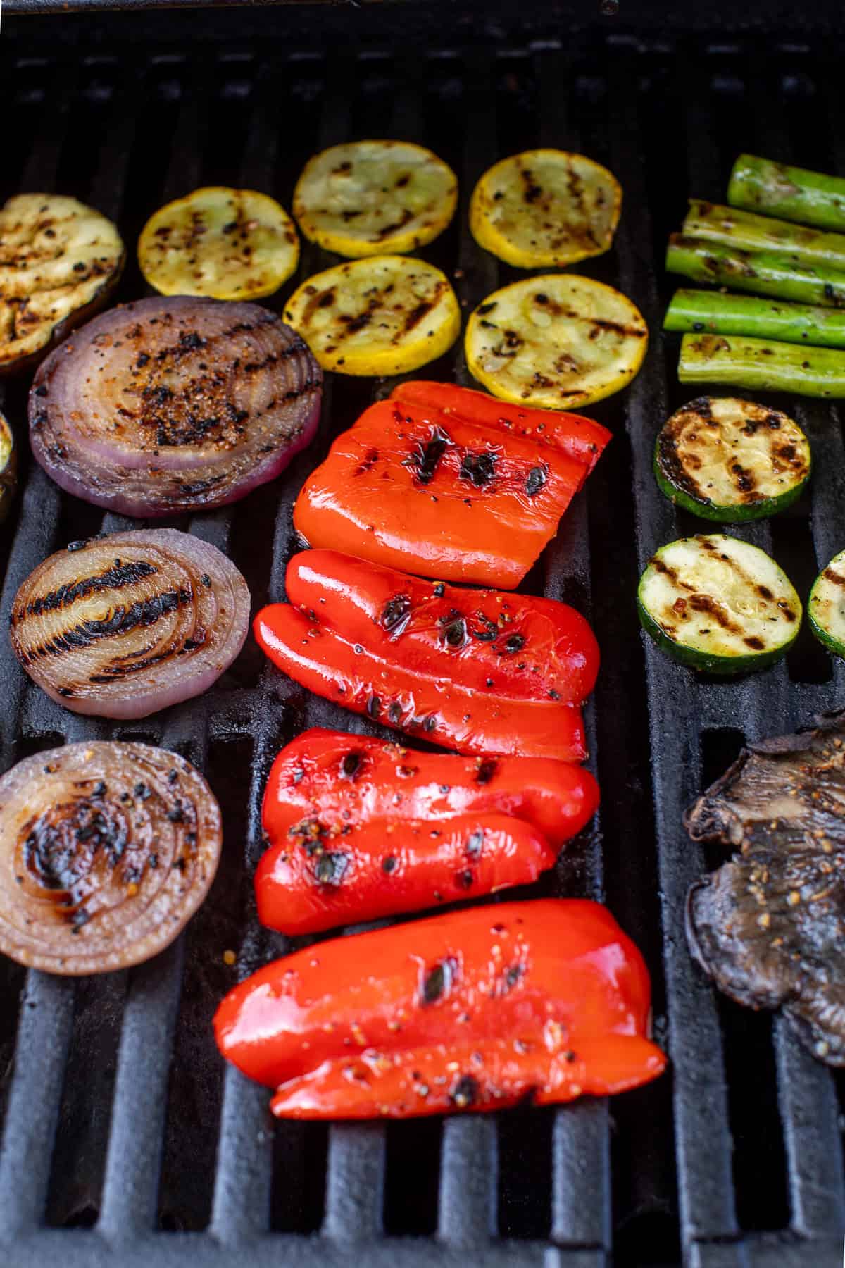 Colorful grilled vegetables—including red bell pepper, onions, zucchini, squash, and asparagus—on a barbecue grill.
