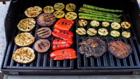 Assorted vegetables, including mushrooms, onions, peppers, zucchini, squash, and asparagus, grilling on a barbecue.